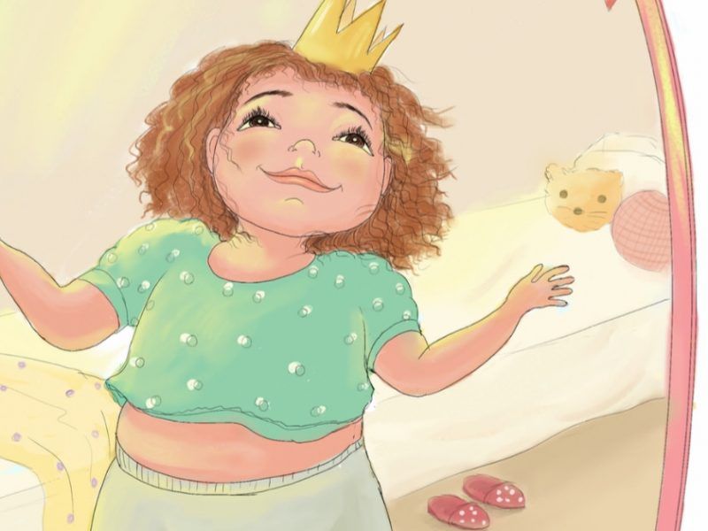 Child wearing a green cropped shirt and a crown gazes at her reflection in the mirror, smiling contentedly.