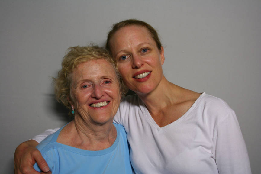 A white woman in a white shirt has her arm around an older white woman in a blue shirt