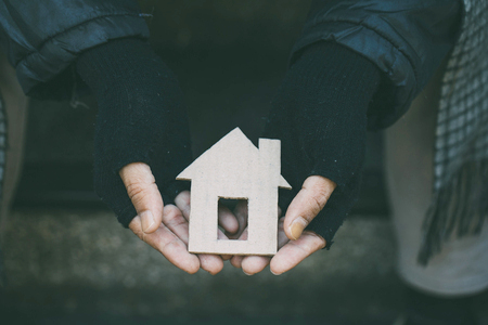 A person wearing black fingerless gloves holds a cardboard cutout in the shape of a house