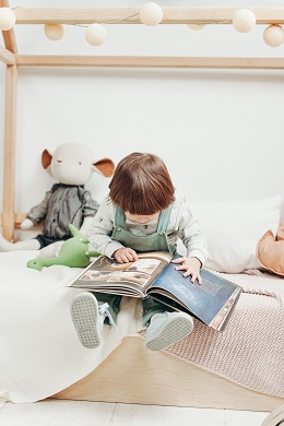 child reading wordless picture book while sitting on bed
